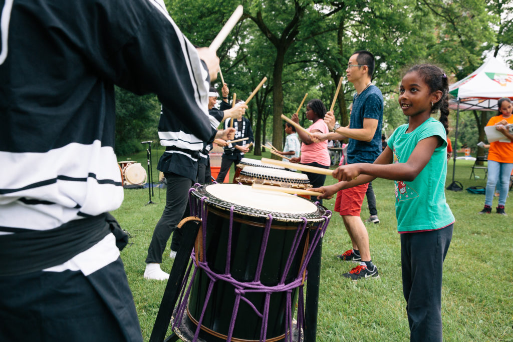 A group of children learn to play the drums in a field.