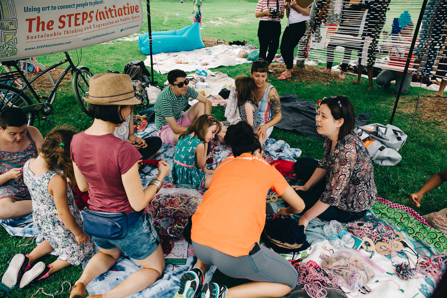 A group of adults and children sitting on blankets under a tree doing crafts together.