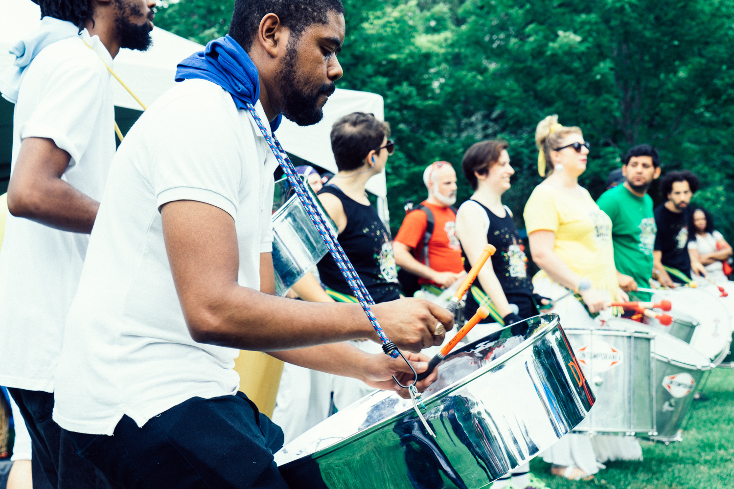A horizontal line of people play steel drums as they march over the grass