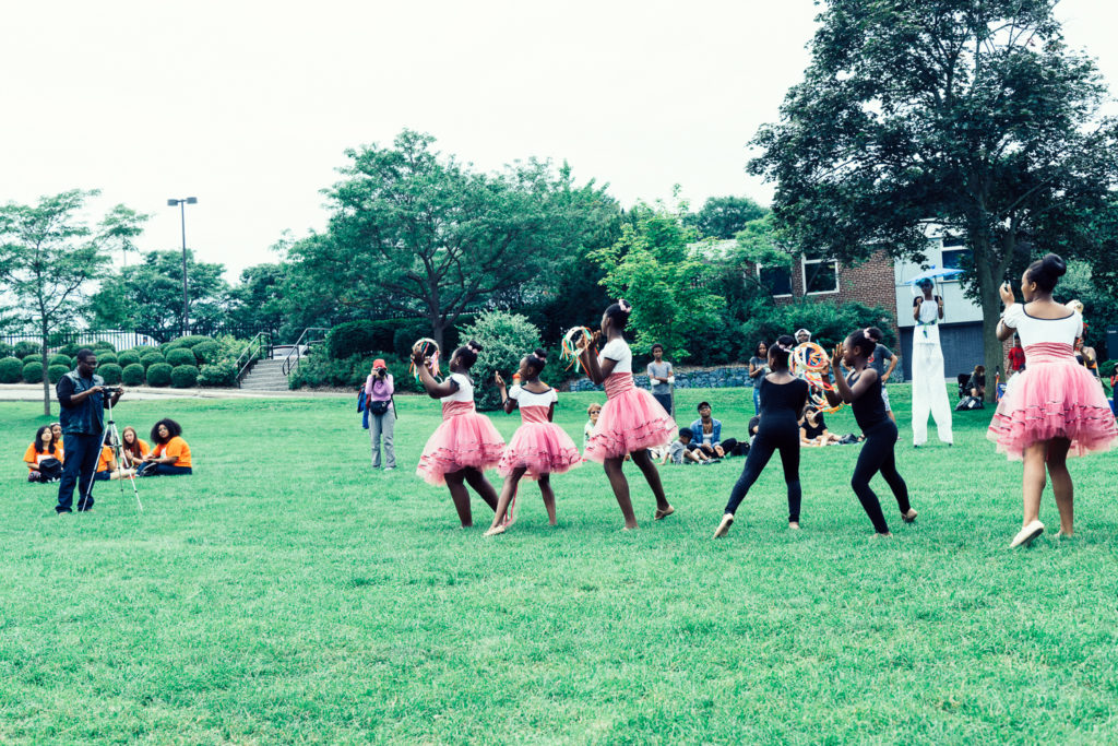 A group of women in bright poofy pink skirts dance in a line across a field.