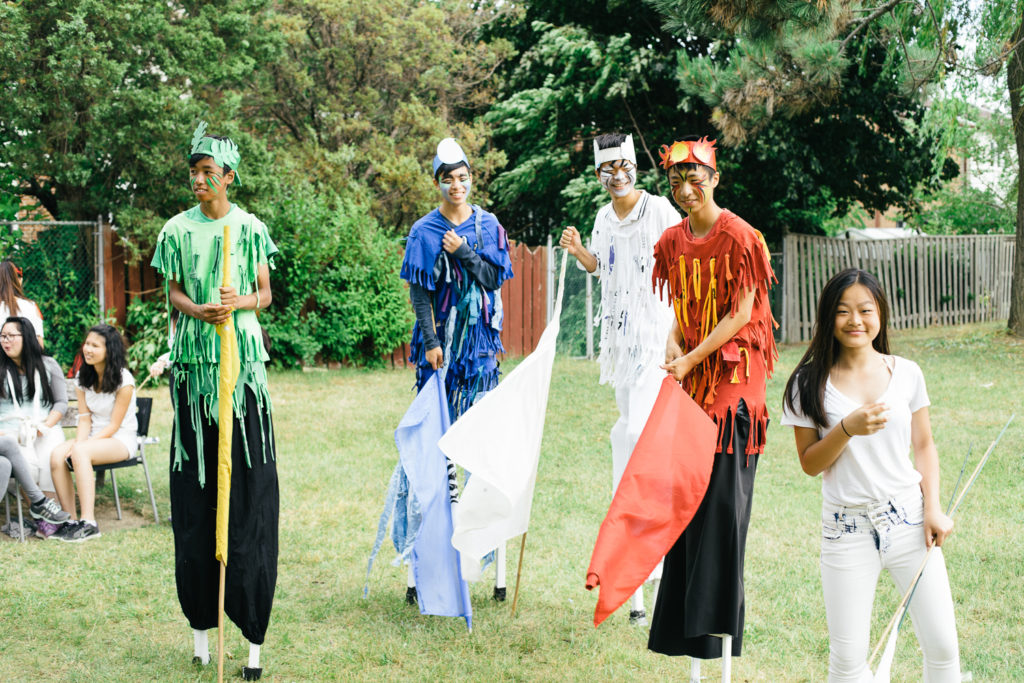 A group of people dressed in colourful costumes walk on stilts.