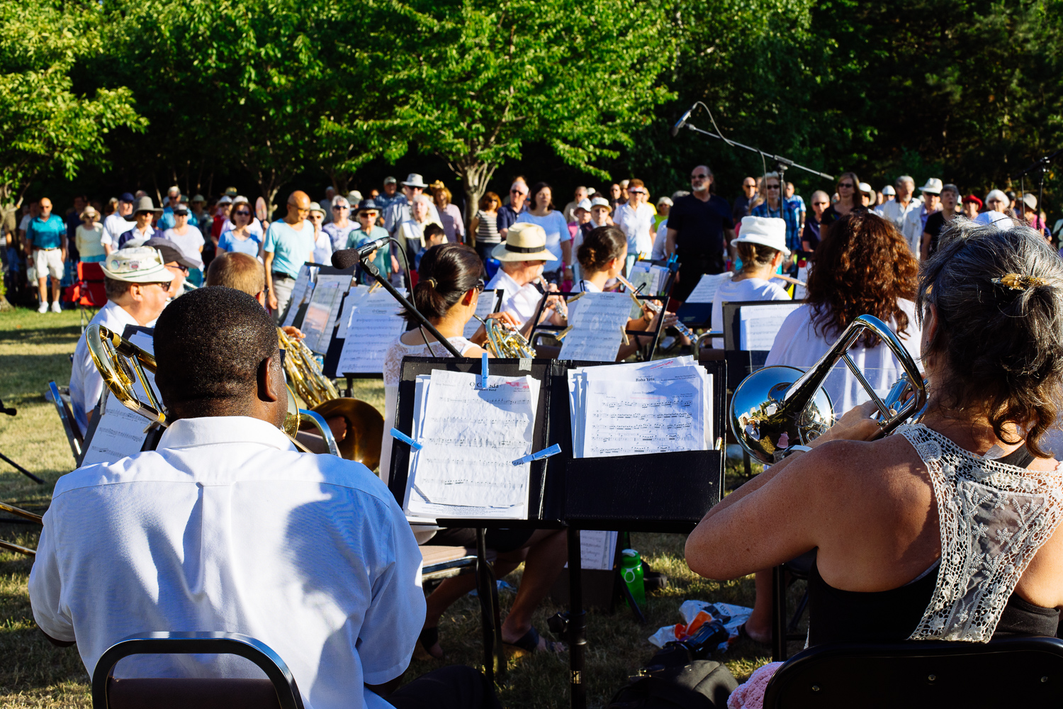 Musicians are seated while playing instruments and reading music, a large audience looks on.