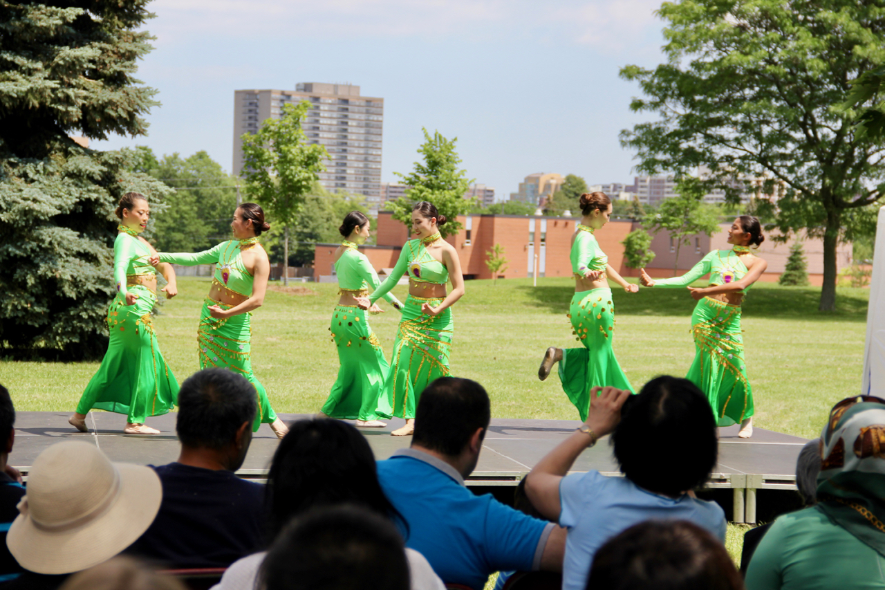 A group of women dancers in bright green costumes dance in pairs on stage.