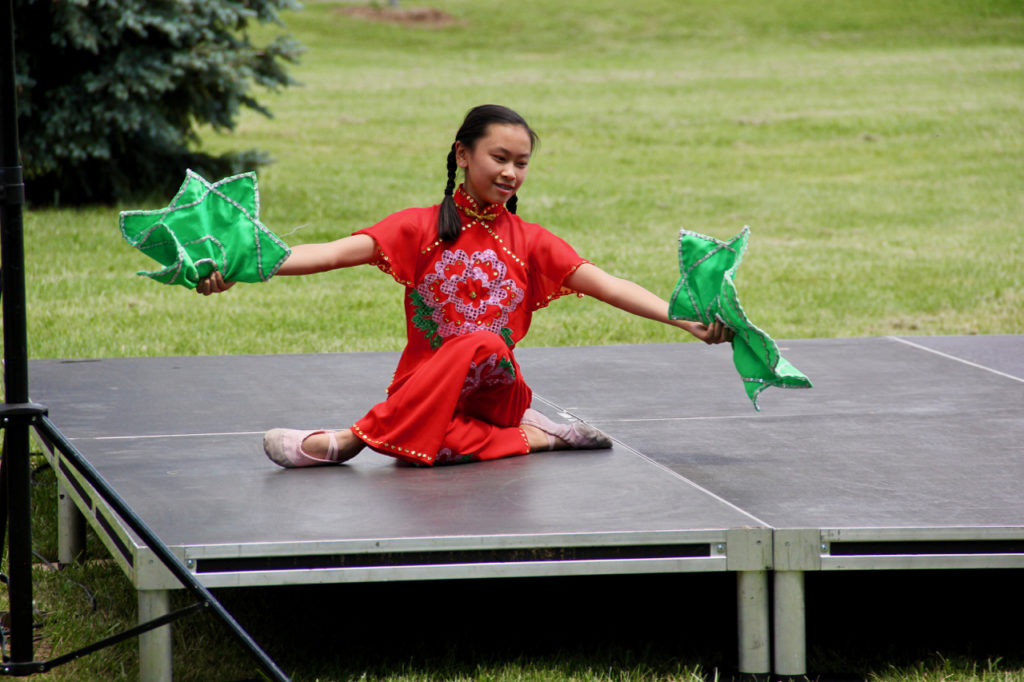 A woman in red dances with two green fans on stage.