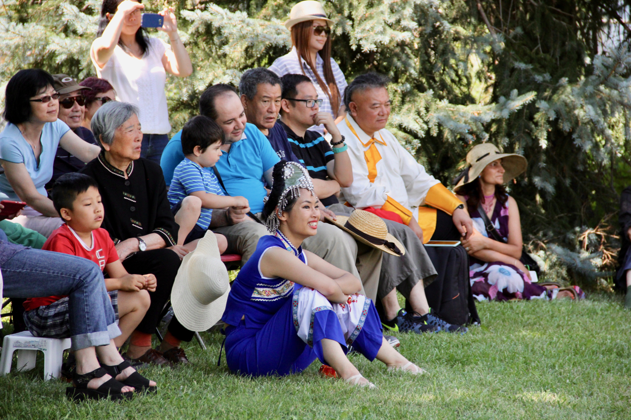 Audience members watch the event seated under the shade of a tree.