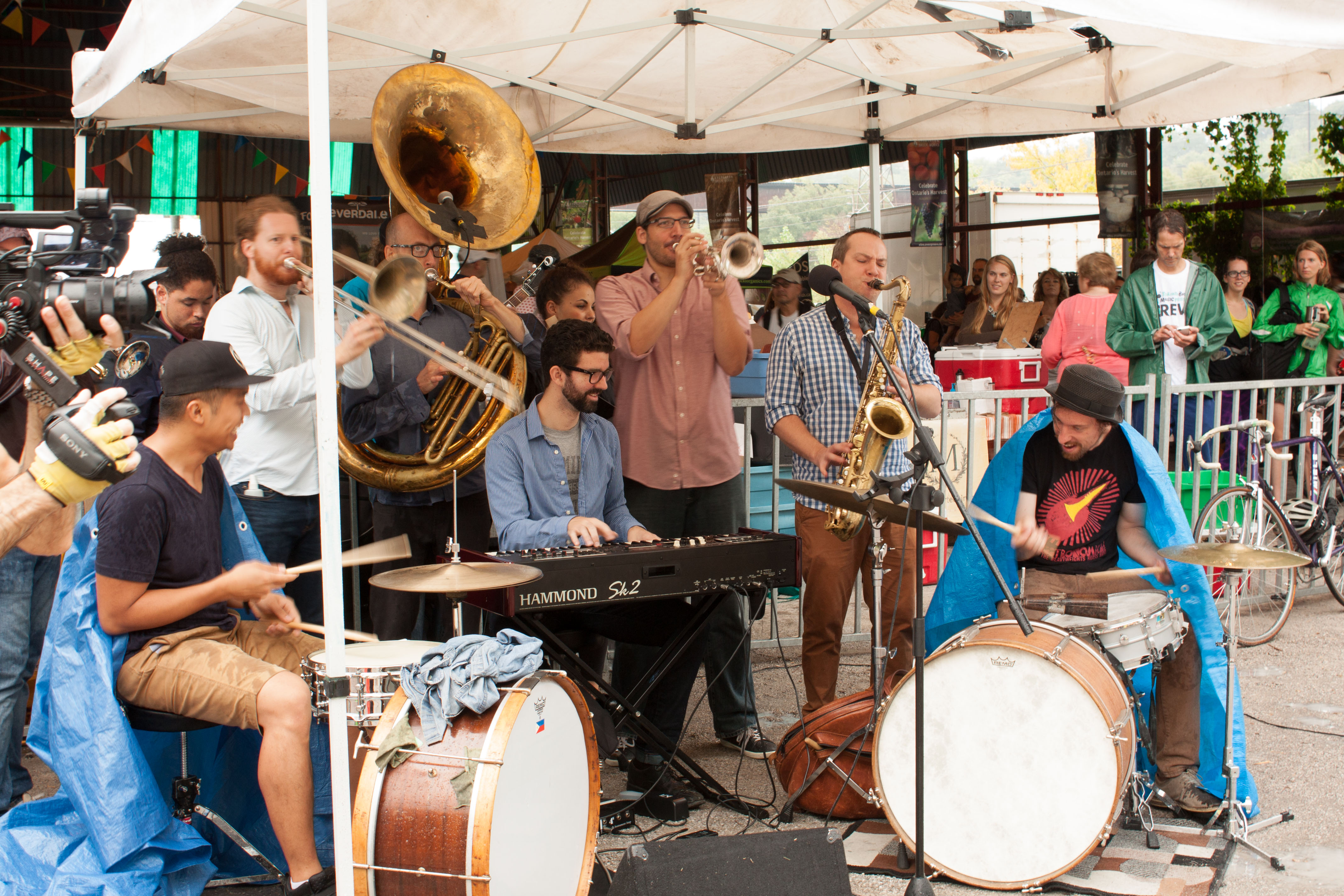 Image description: a band plays various instruments and smiles as they perform under a tent.