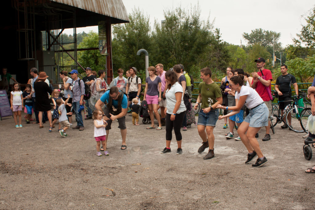 Image description: a group of participants dance to music on a dirt surface.