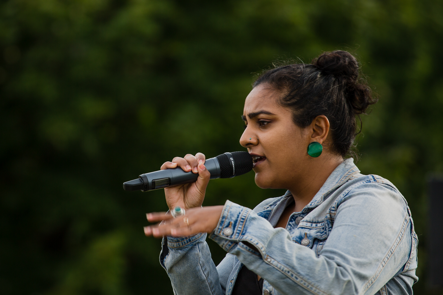 A woman in a jean jacket sings into a microphone.