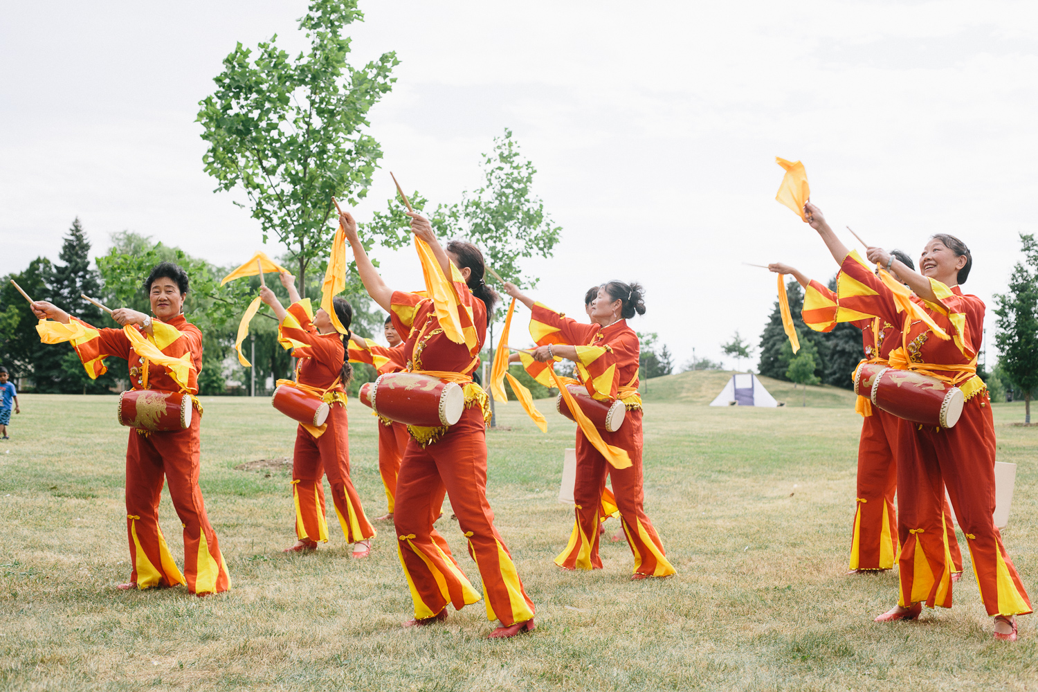 A group of women dancers in yellow and red costumes carry drums as they move across a field.