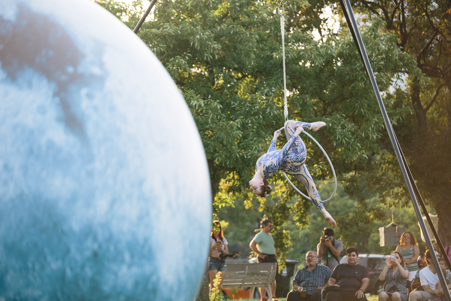 A large blue sphere sits in the foreground while a woman dances in a hanging hoop in the background.