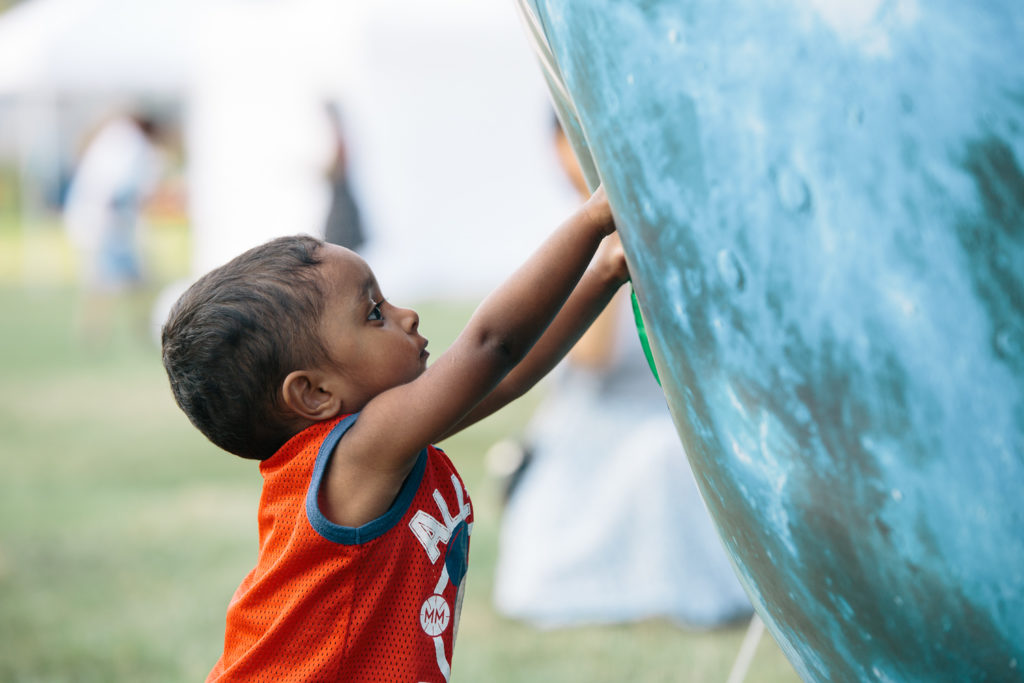 A small child places his hands on a giant blue sphere.