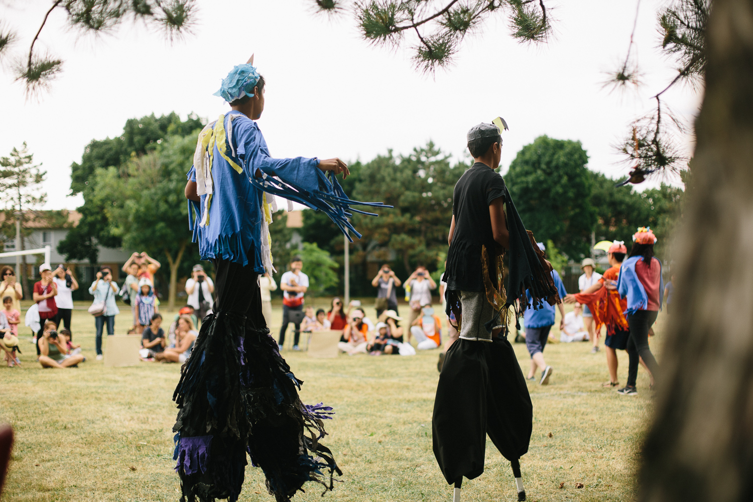 Two performers in costume on stilts through a field.