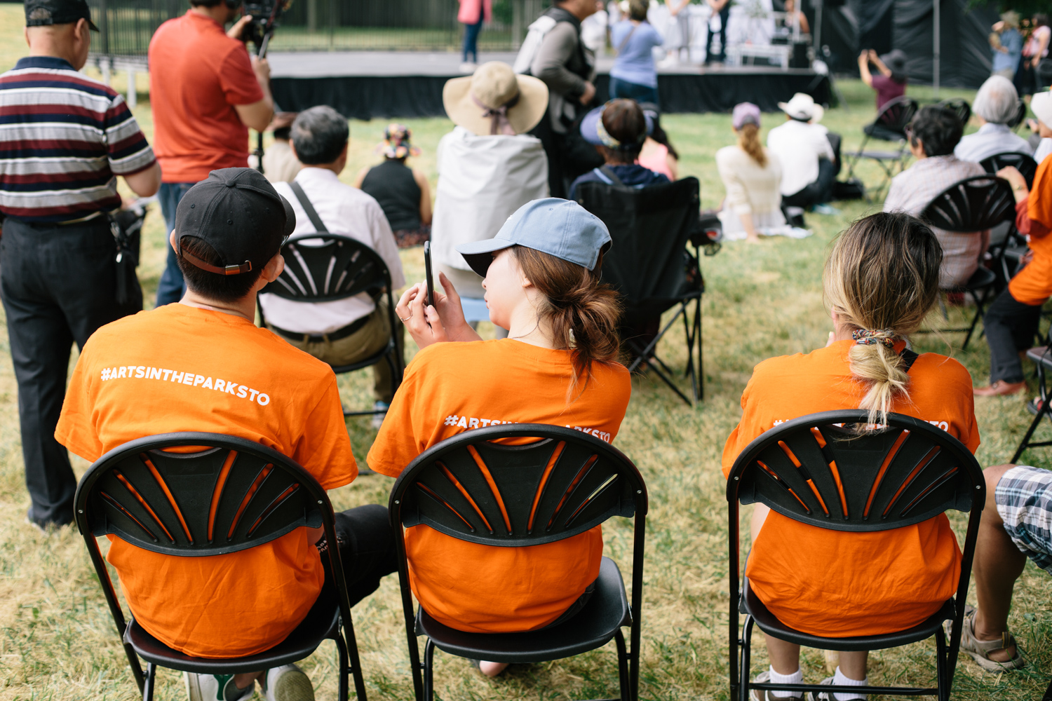 Three volunteers in orange shirts sit in chairs with the audience.