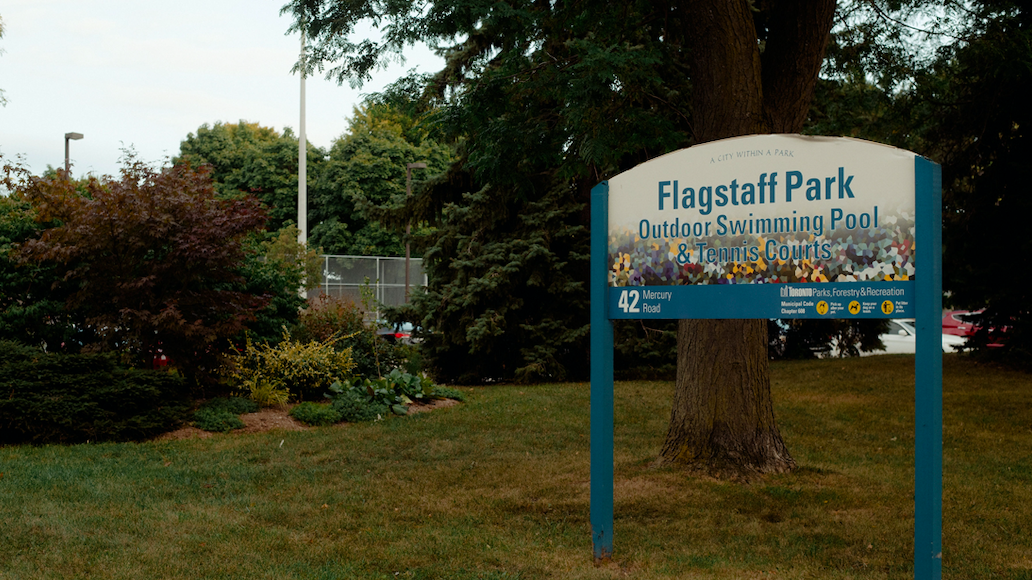 Sign that says "Flagstaff Park" stands to the right in front of a tree and some bushes.