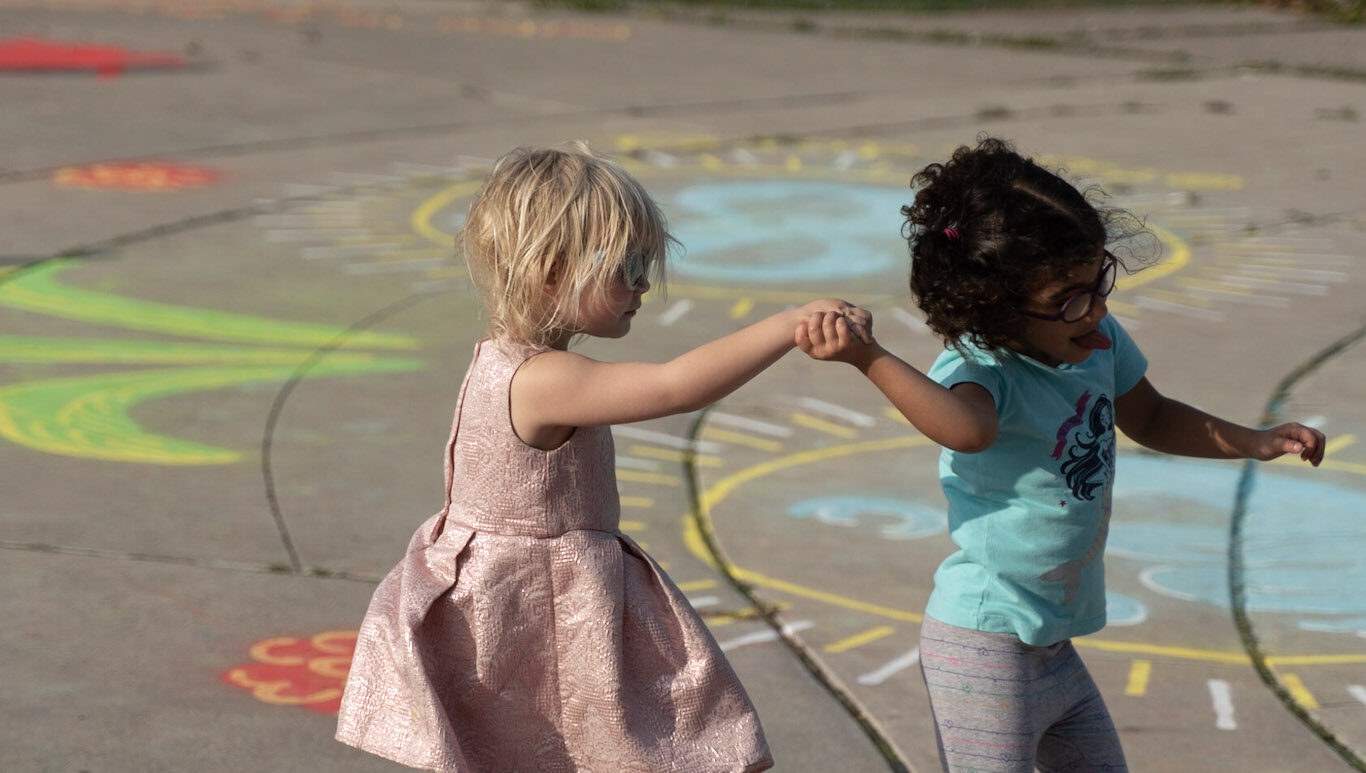 Two children dance with each other on pavement that has been colourfully painted.