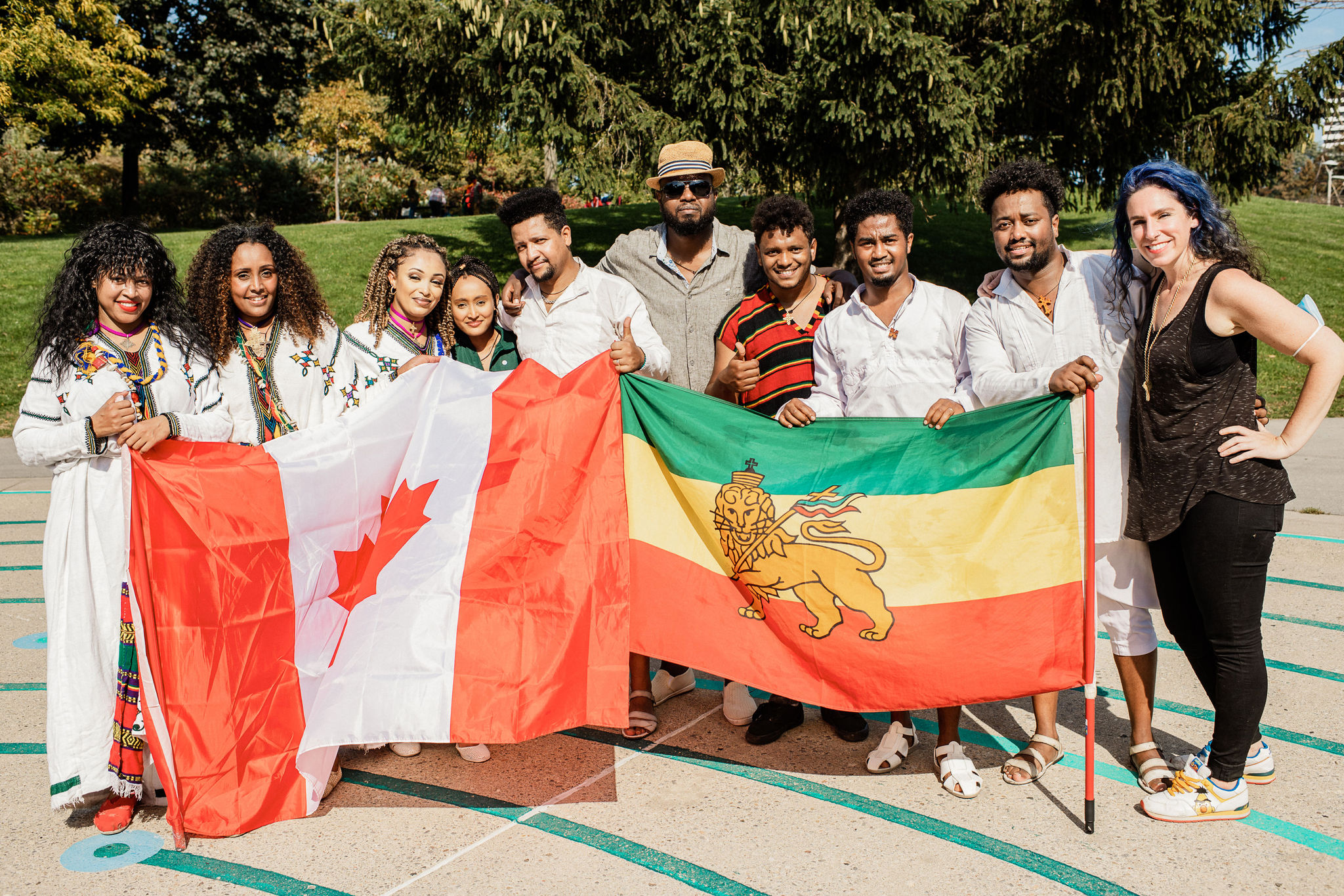 Performers stand next to each other holding up a Canadian flag and Ethiopian flag next to each other. They look directly at the camera and smile.