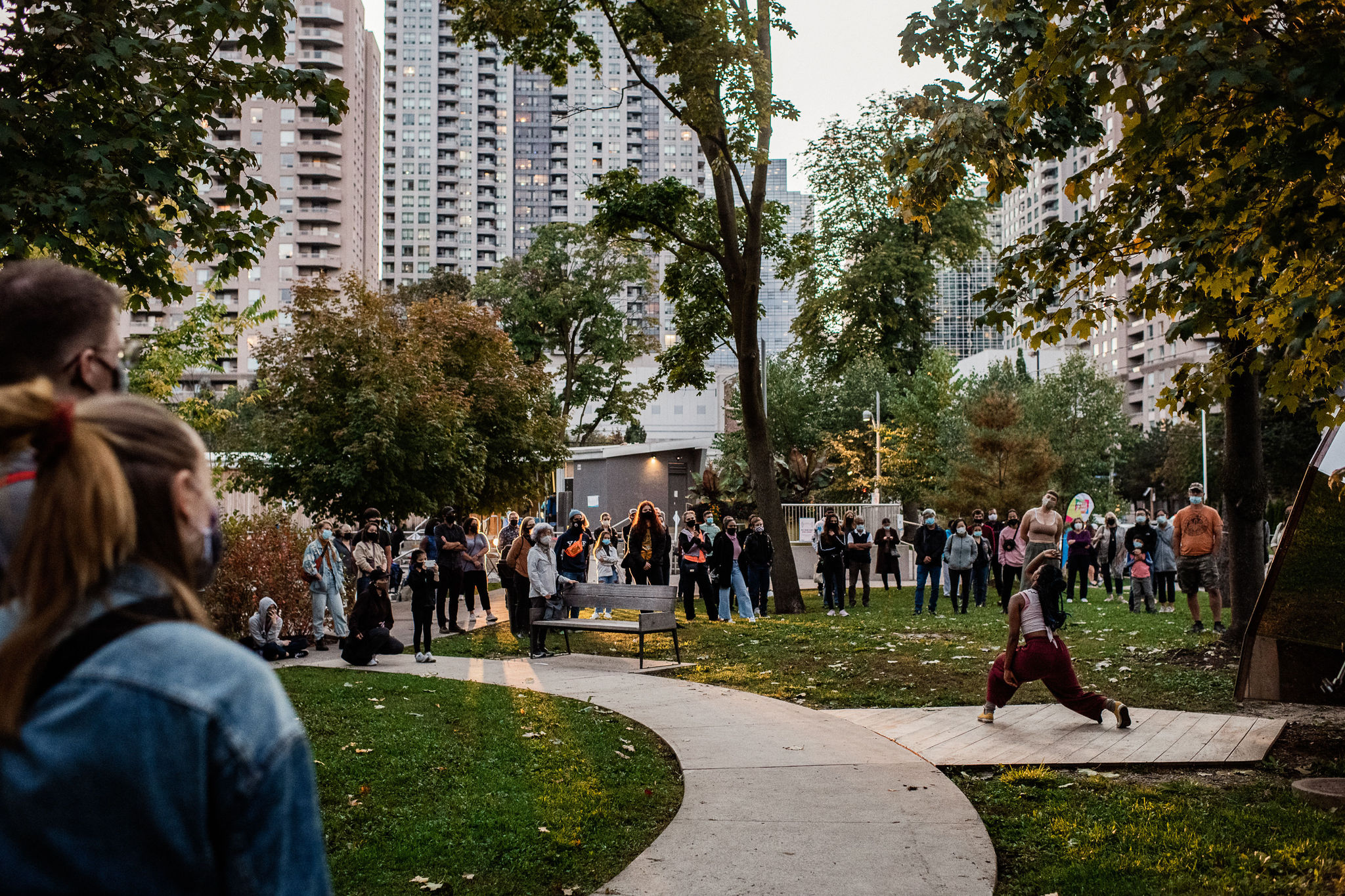 A woman dances on a sidewalk while audience members stand and form a circle around her.