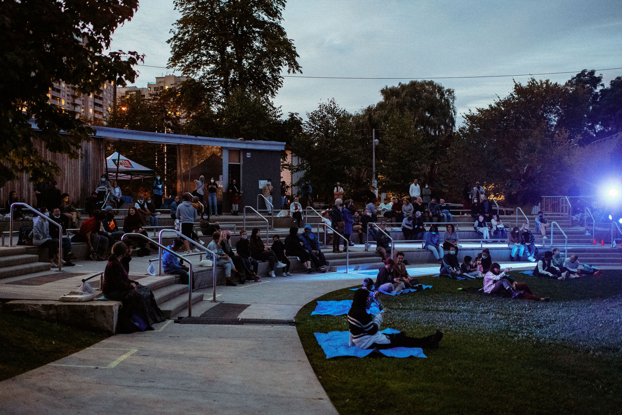 Audience members sit on concrete tiered seating in front of lights as they wait for a performance to beghin.