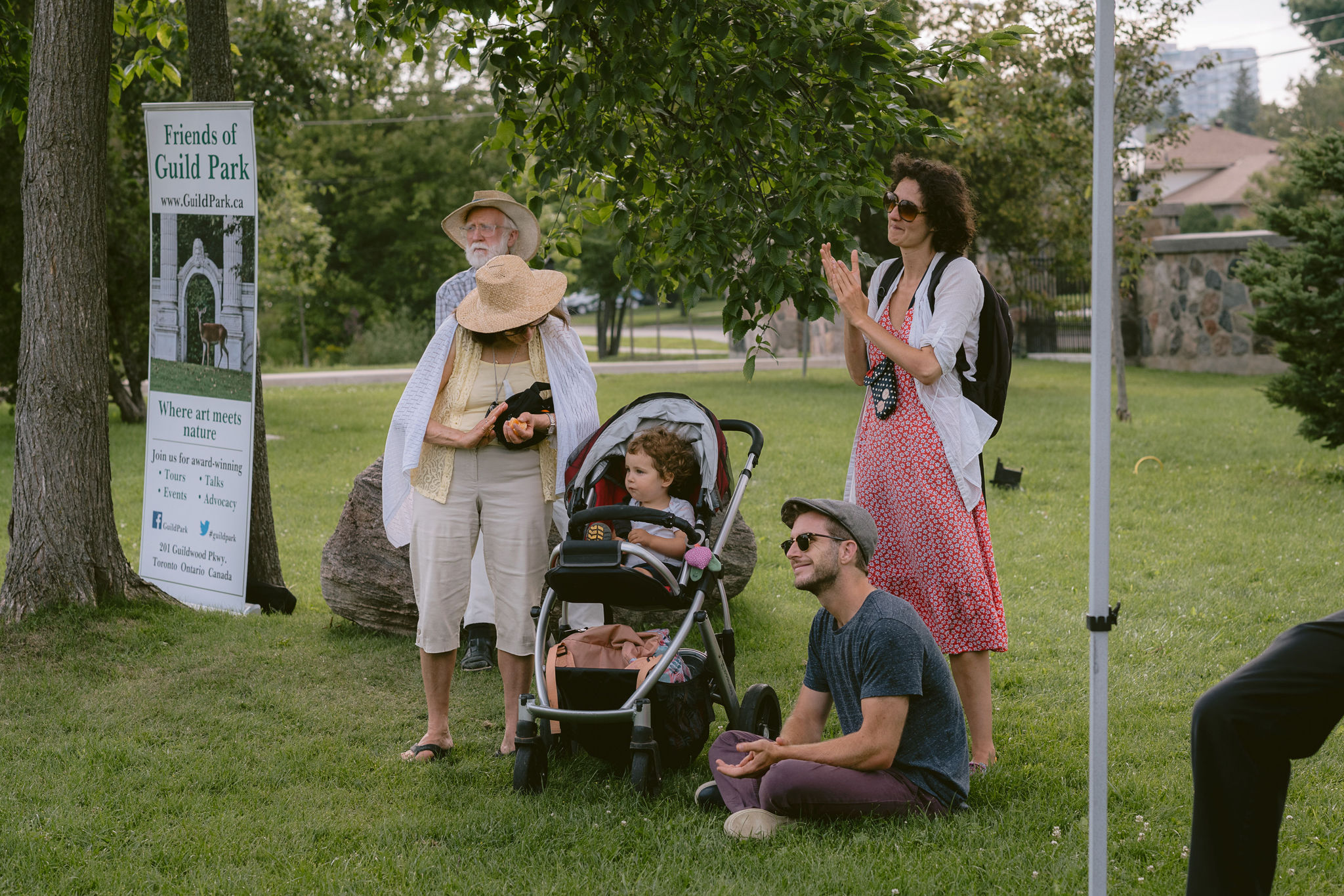 A family watches a Tapestry Opera Box Concert, with a Friends of Guild Park sign in the background.