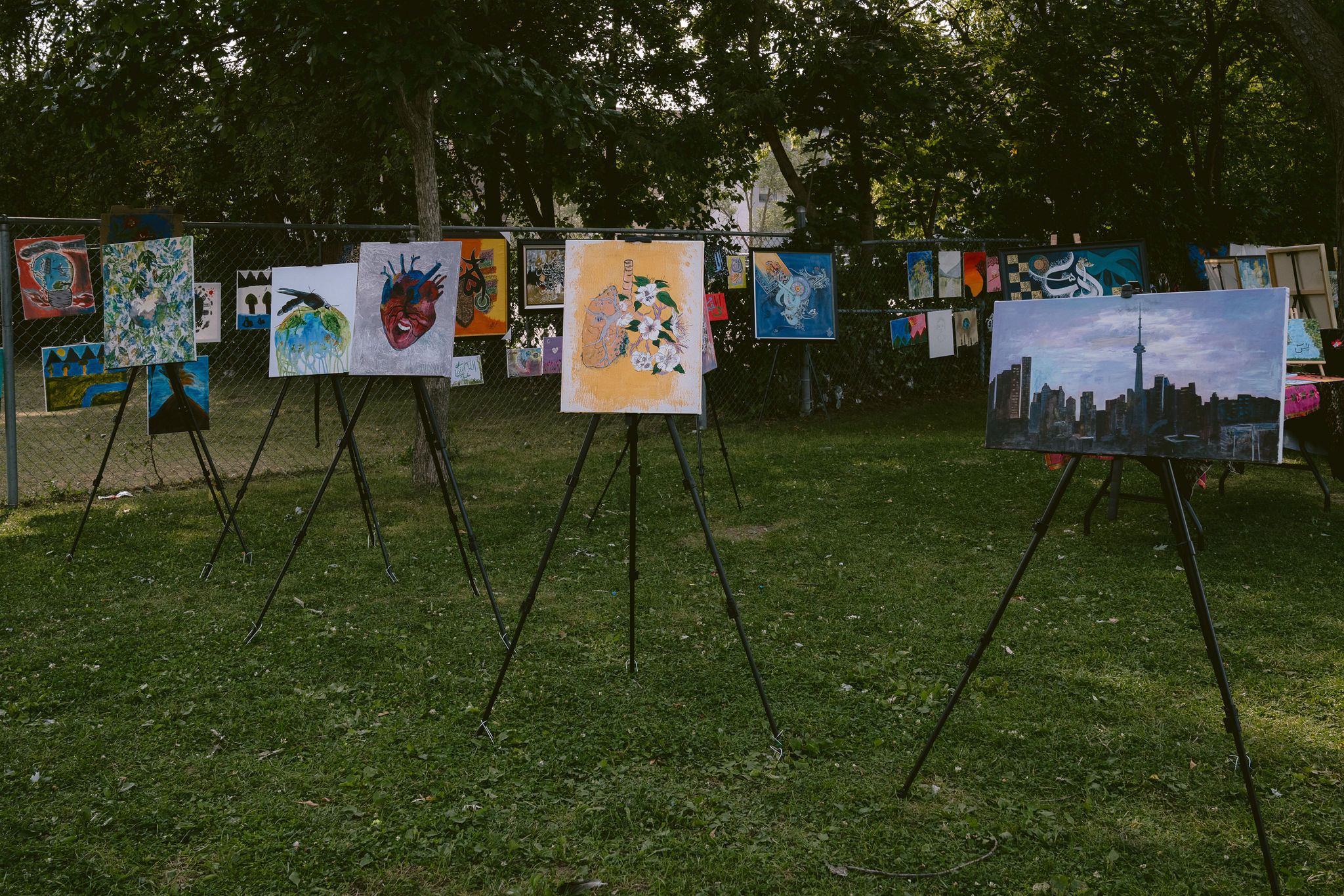 Artworks displayed on easels and fences in the park.