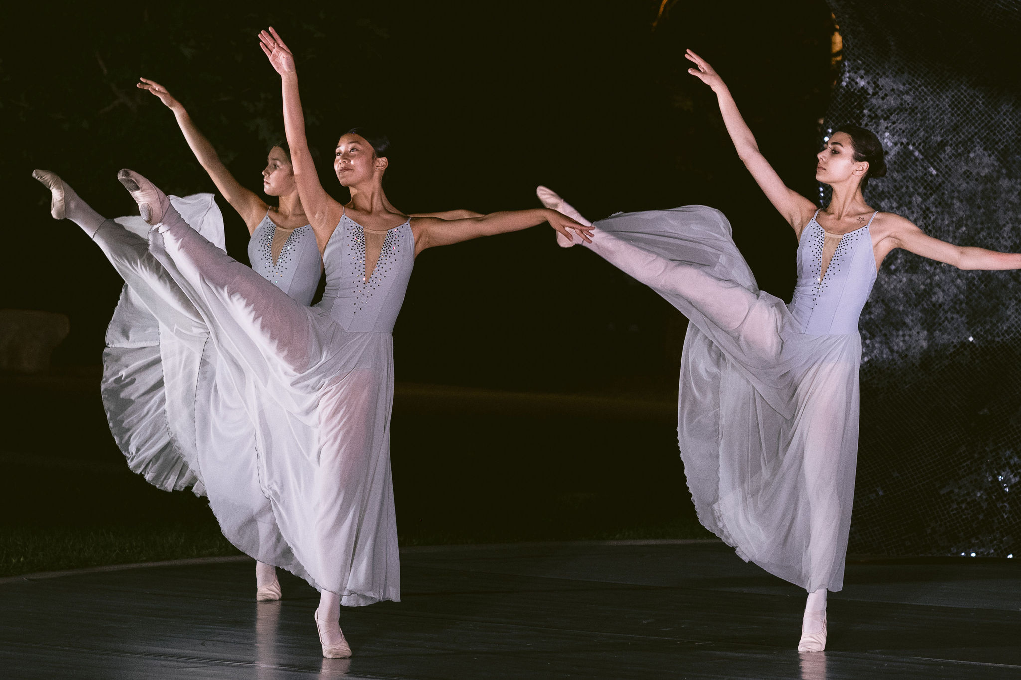 Three ballerinas in white costumes dance on stage