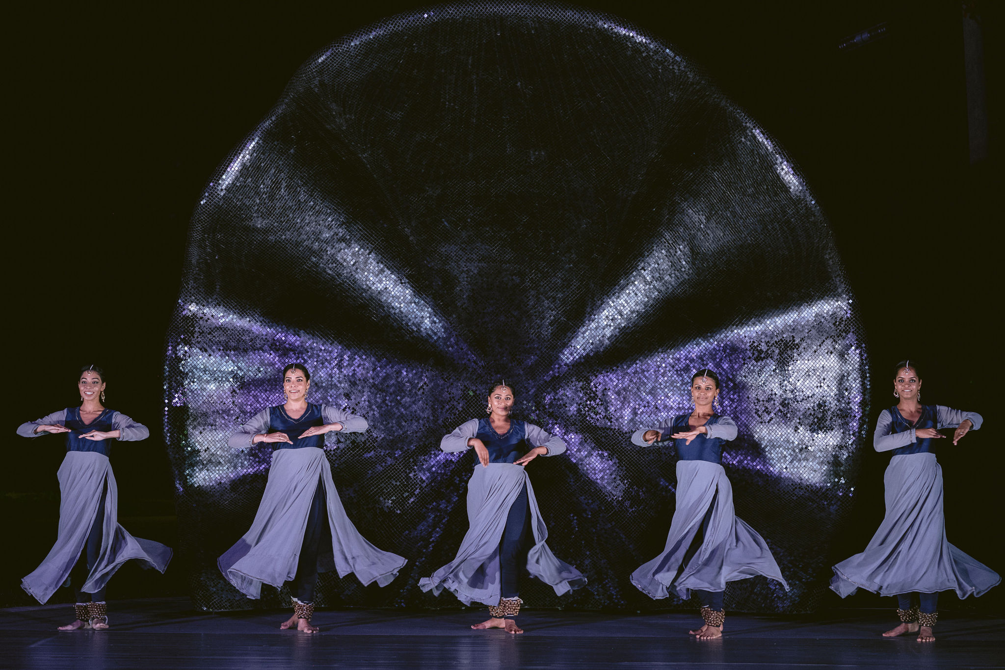 Five women in blue dresses dance on stage